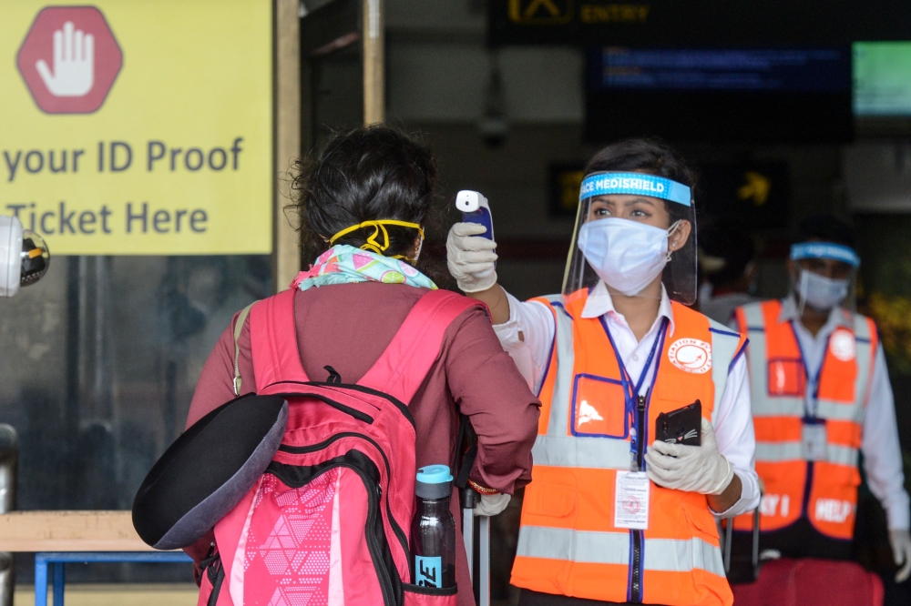 An airport employee (C) wearing a face shield checks the body temperature of a passenger at Bagdogra airport after the goverment eased a nationwide lockdown imposed as a preventive measure against the COVID-19 coronavirus, on the outskirts of Siliguri on 