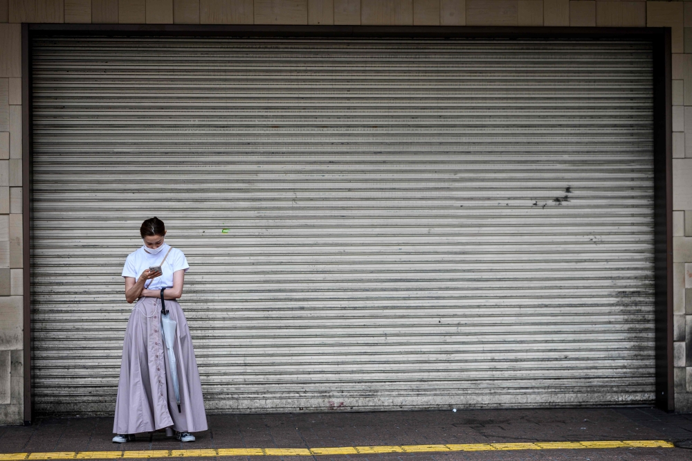 A woman wearing a face mask amid concerns over the spread of the COVID-19 coronavirus uses her phone as she stands in front of a closed department store in Tokyo on May 26, 2020. AFP / Behrouz MEHRI