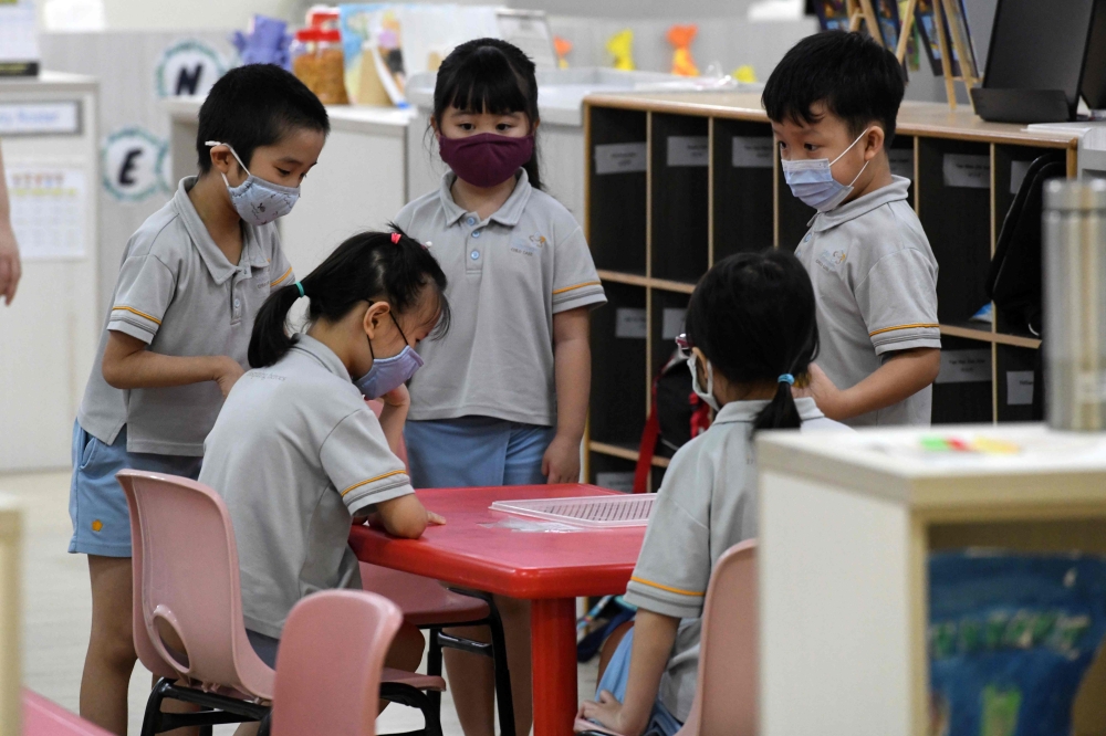 Children wearing face masks gather around a table inside their classroom as schools reopened in Singapore on June 2, 2020, as the city state eased its partial lockdown imposed to prevent the spread of COVID-19 in Singapore. / AFP / ROSLAN RAHMAN