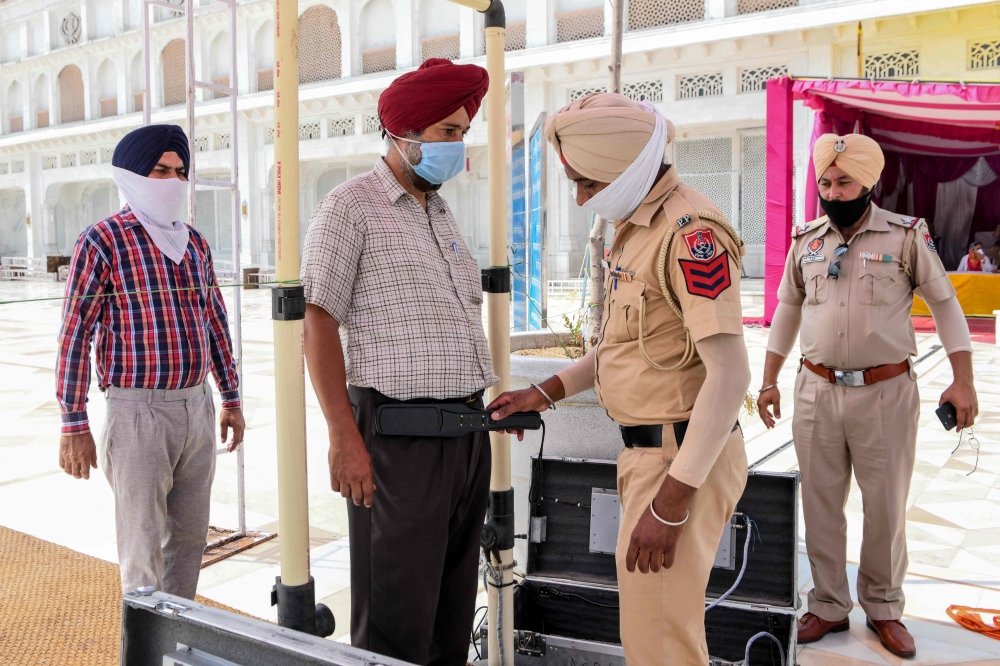 A police personnel (2R) checks a Sikh devotee (2L) as he arrives at the Golden Temple ahead of the 36th Operation Blue Star anniversary in Amritsar on June 5, 2020.  / AFP / NARINDER NANU
