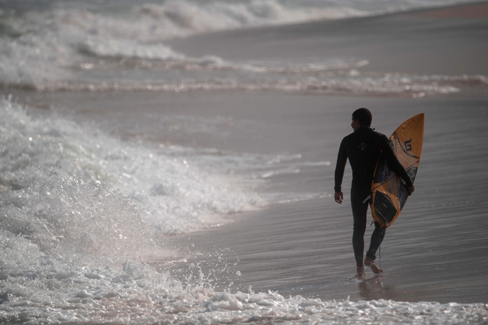A surfer walks at the Arpoador beach in Rio de Janeiro state, Brazil, on June 02, 2020, during the new coronavirus COVID-19 pandemic. / AFP / MAURO PIMENTEL
