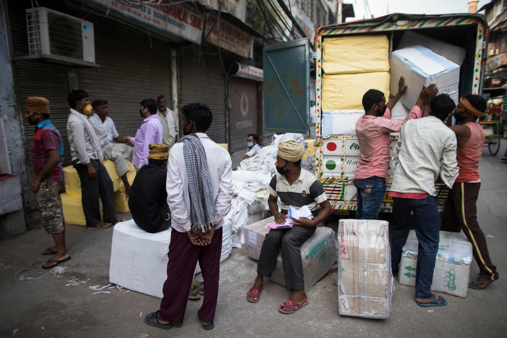 Workers gather outside a shop while others load a vehicle after the government eased a nationwide lockdown imposed as a preventive measure against the COVID-19 coronavirus, in the old quarters of New Delhi on June 5, 2020. / AFP / XAVIER GALIANA