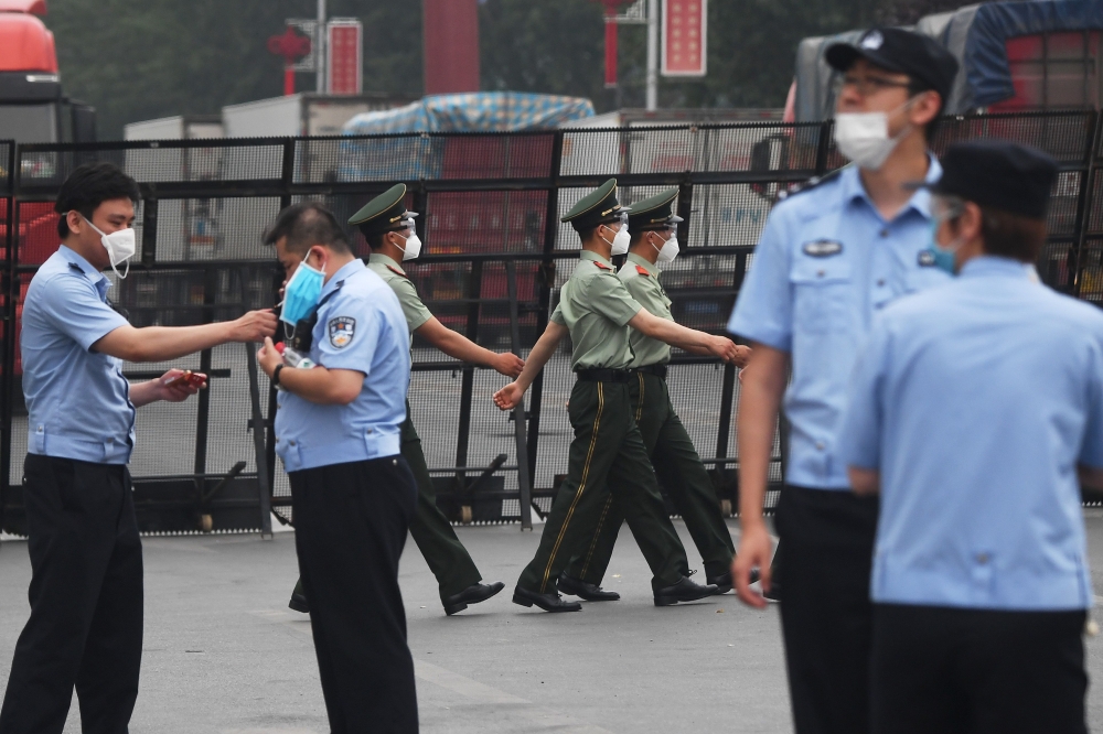 Paramilitary police officers (C) march as police stand guard at the entrance to the closed Xinfadi market in Beijing on June 13, 2020. AFP / GREG BAKER