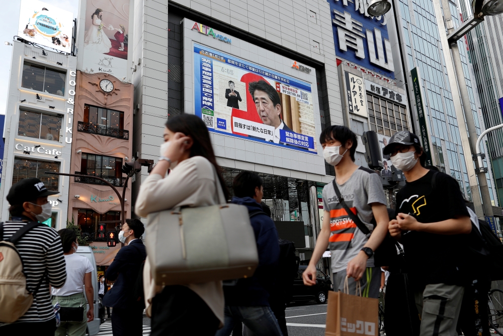 FILE PHOTO: A large screen on a building shows live broadcast of Japan's Prime Minister Shinzo Abe's news conference on the lifting of the state of emergency in Tokyo and the remaining 5 areas still under alert for the coronavirus disease (COVID-19) at Sh