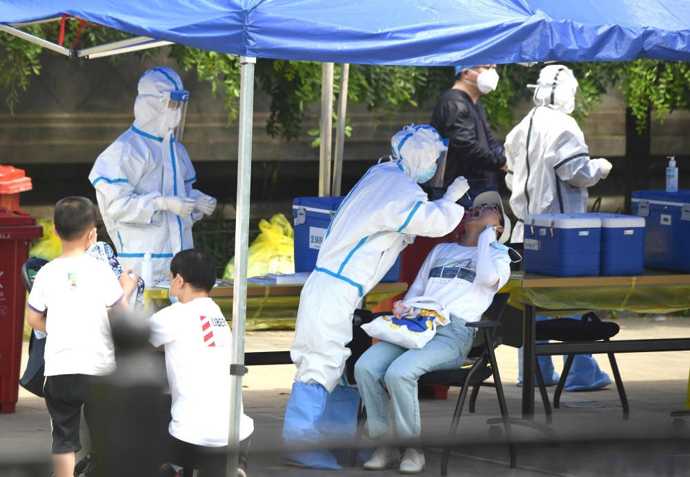 A health worker (2nd-L) wearing a protective suit takes a swab test on a woman in Beijing on June 16, 2020. AFP / Noel Celis