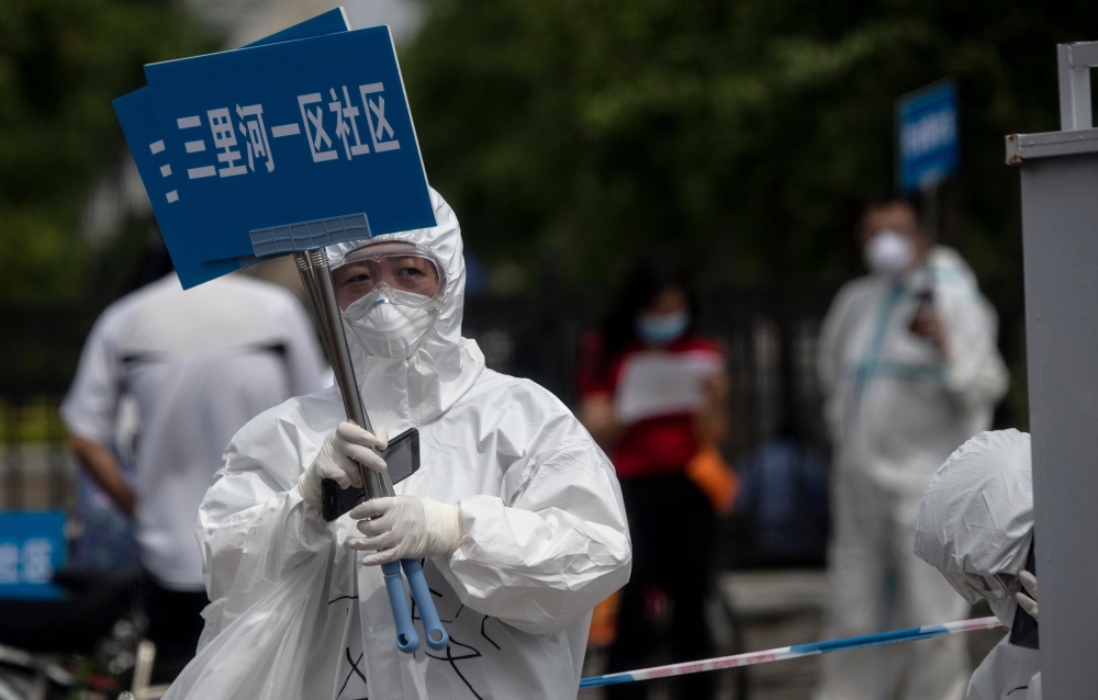 Medical staff in full protective gear carry signs to assist people who live near or who have visited the Xinfadi Market, a wholesale food market where a new COVID-19 coronavirus cluster has emerged, as they arrive for testing in Beijing on June 17, 2020. 