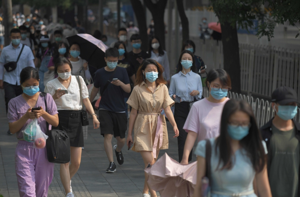 People wear masks as they walk to work in Beijing on June 28, 2020. Beijing has partially lifted weeks-long lockdown imposed in the Chinese capital to head off a feared second wave of coronavirus infections after three million samples were taken in two we