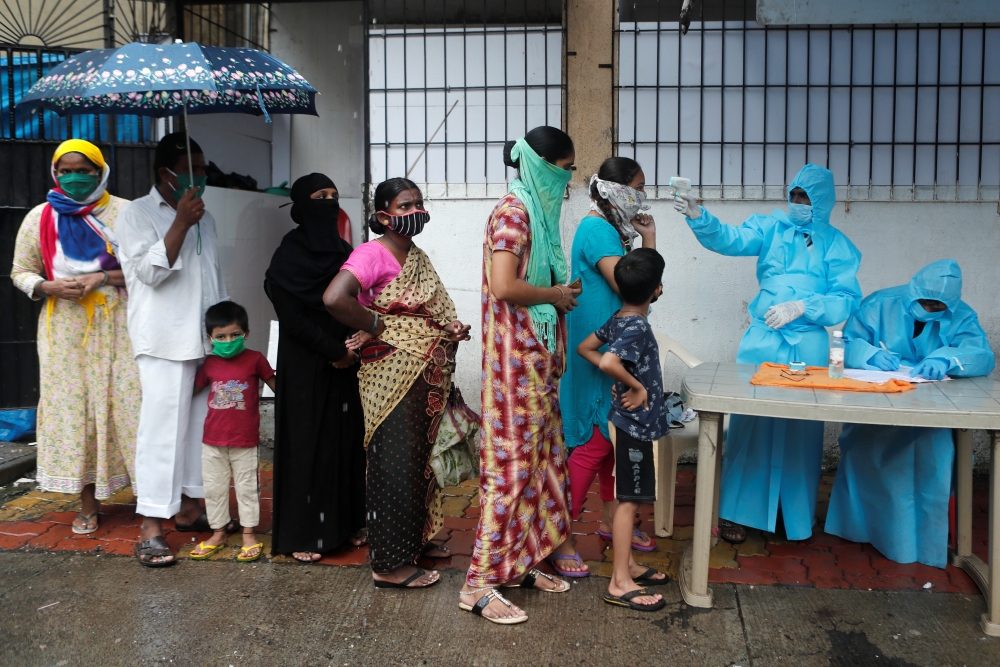 People stand in a queue as a healthcare worker checks the temperature of a resident using an electronic thermometer during a medical campaign for the coronavirus disease (COVID-19) in Mumbai, India, July 4, 2020. REUTERS/Francis Mascarenhas