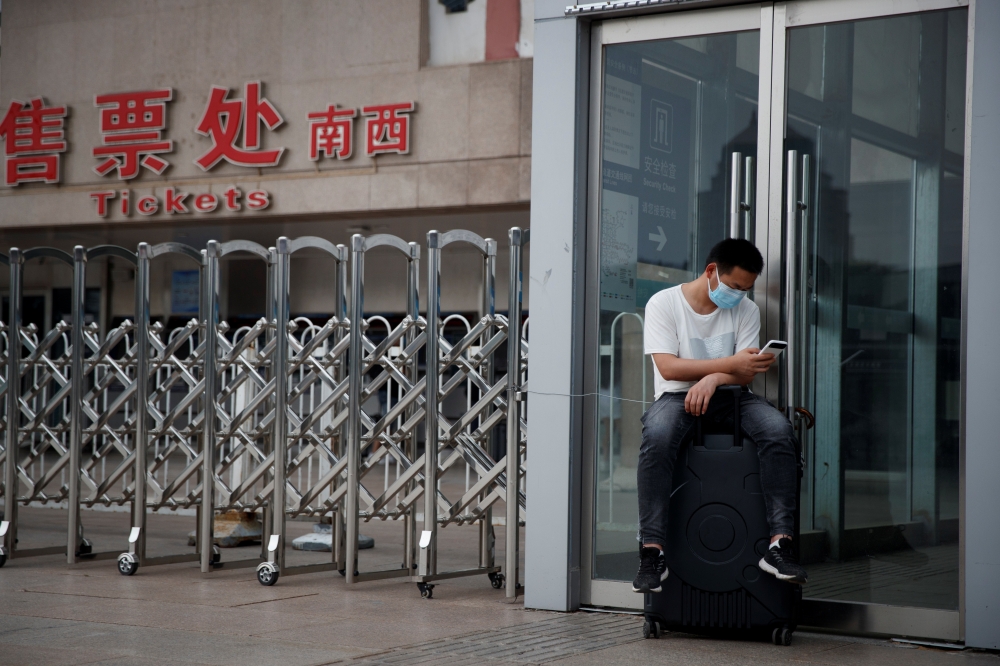 A man wears a protective mask as he sits on his suitcase at the Beijing West Railway Station, after an outbreak of the coronavirus disease (COVID-19), in Beijing, China July 3, 2020. REUTERS/Thomas Peter