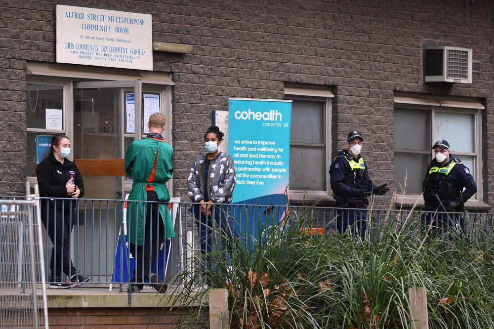 Police and medical workers stand outside an entrance to a public housing estate which is undergoing a forced lockdown in Melbourne on July 10, 2020, as the city records another 288 new cases in a fresh outbreak of the COVID-19 coronavirus.  AFP / William 