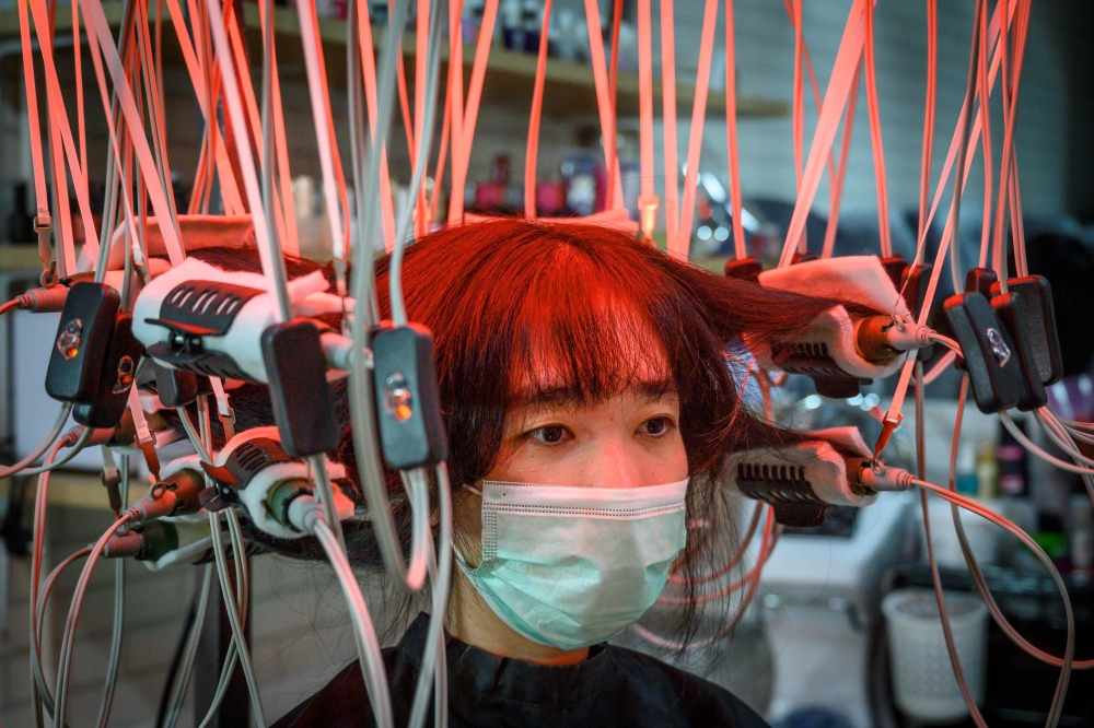 A woman wearing a face mask has her hair curled by a special equipment at a beauty salon in Bangkok on July 12, 2020. / AFP / Mladen ANTONOV