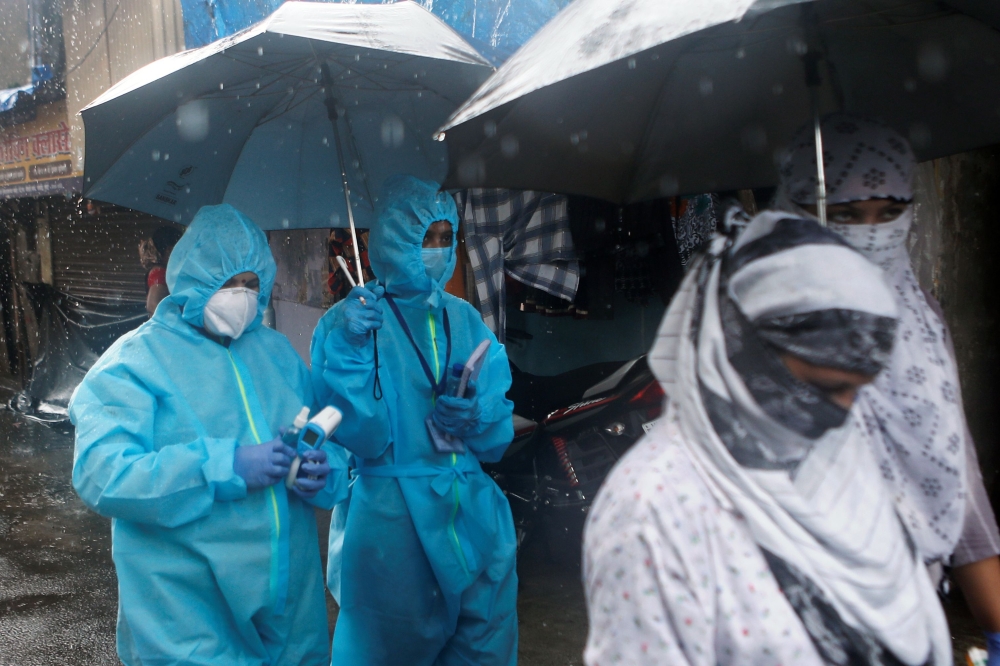 A health worker in personal protective equipment (PPE) walks holding an umbrella on a rainy day during a check up campaign for the coronavirus disease (COVID-19) in Mumbai, India, July 14, 2020. REUTERS/Francis Mascarenhas