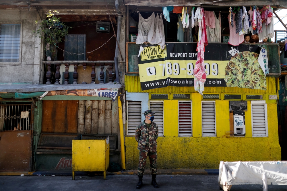 A soldier wearing a protective mask guards a street while children look out from a balcony, as the city undergoes a stricter lockdown to contain the coronavirus disease (COVID-19) spread, in Pasay City, Philippines, April 22, 2020. REUTERS/Eloisa Lopez/Fi