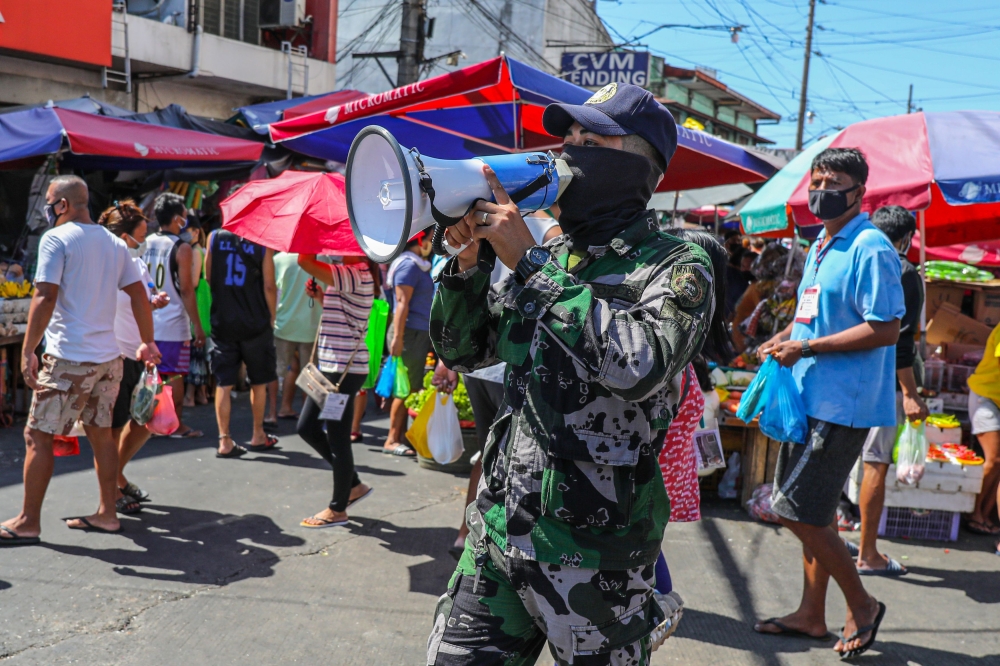 In this file photo taken on April 21, 2020, a member of the Philippine National Police Special Action Forces uses a megaphone to remind shoppers to practice social distancing during a government imposed enhanced quarantine as a preventive measure against 