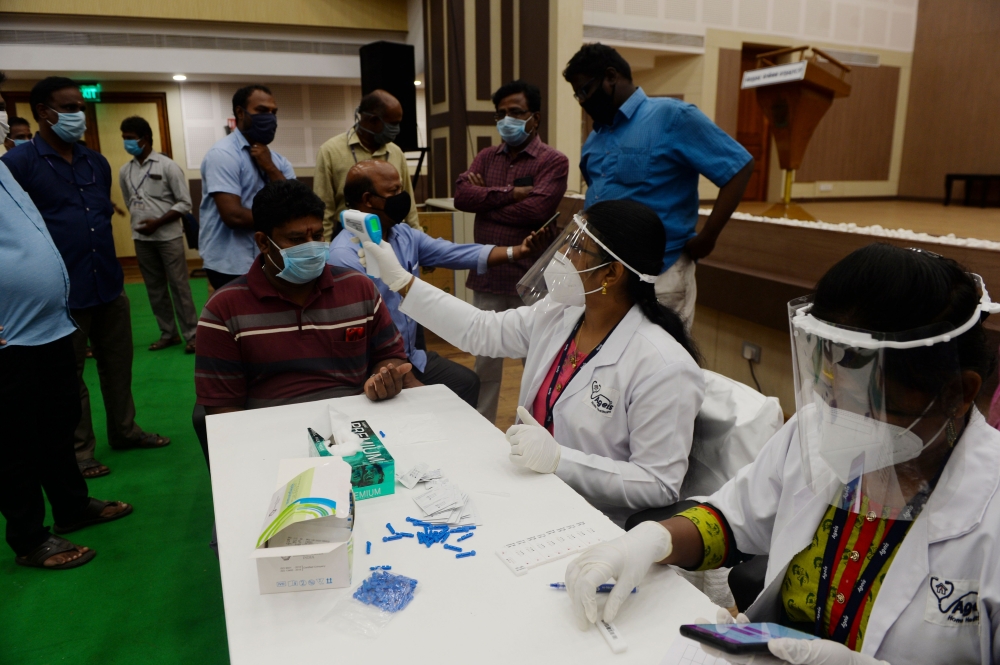 A medical technician (C) takes the body temperature of a man before taking a sample for a COVID-19 anti-body tests at a temporary testing facility for frontline workers during a lockdown as a preventive measure against the COVID-19 coronavirus in Chennai 