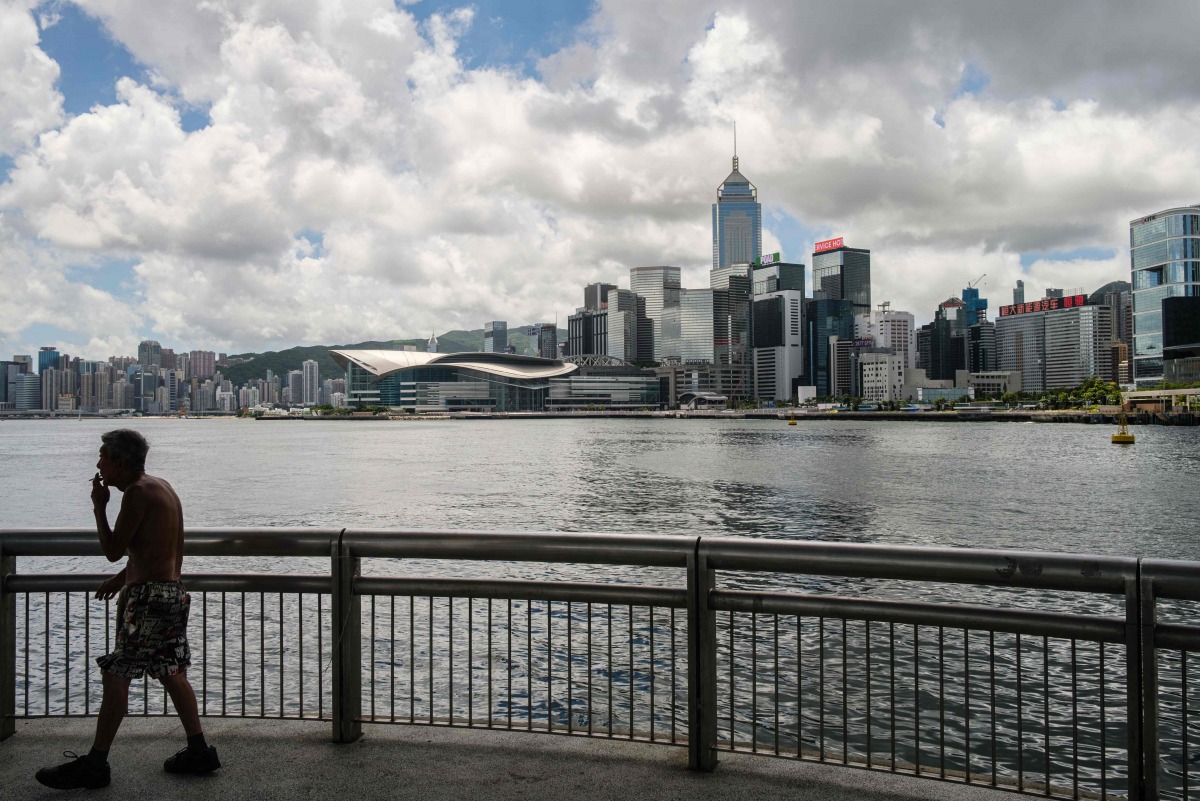A man walks on a pier in Victoria Harbour past a view of commercial buildings in Hong Kong on July 16, 2020. / AFP / Anthony WALLACE / 