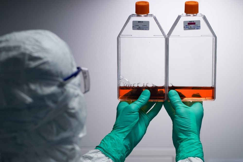 A lab technician wearing Personal Protective Equipment (PPE) looks at reagent bottles before performing vaccine tests at a French pharmaceutical company Sanofi's laboratory in Val de Reuil on July 10, 2020. / AFP / JOEL SAGET
