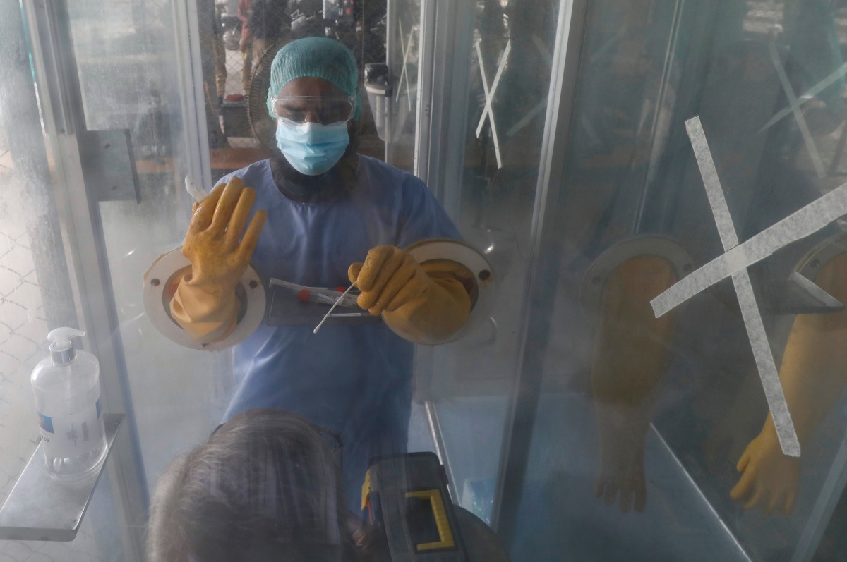 A paramedic wearing protective gear instructs a man while taking nasal swab sample at a glass booth, to be tested for the coronavirus disease (COVID-19), in Karachi, Pakistan July 15, 2020. REUTERS/Akhtar Soomro
