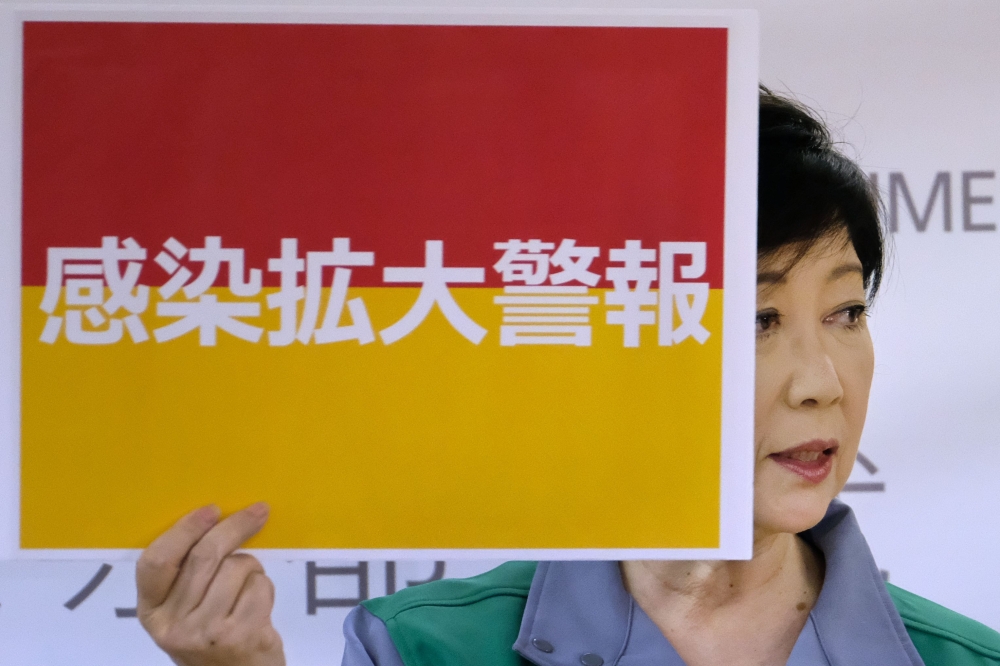 This picture taken on July 15, 2020 shows Tokyo Governor Yuriko Koike displaying a sign reading 'Infection spread alert' during a press conference at the Tokyo Metropolitan Government office. Koike said there were 293 new COVID-19 infections in the capita