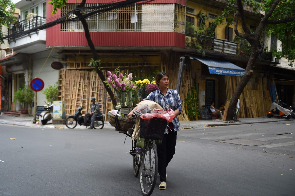A street vendor selling flowers crosses the street with her bicycle in the old district of Hanoi on July 20, 2020. AFP / Nhac Nguyen 