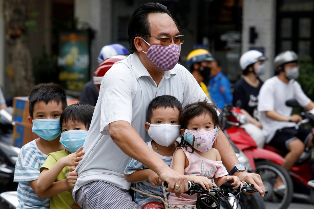 A man and his children, all wearing protective masks, ride a bicycle on a street during the coronavirus disease (COVID-19) outbreak, in Hanoi, Vietnam July 27, 2020. REUTERS/Kham