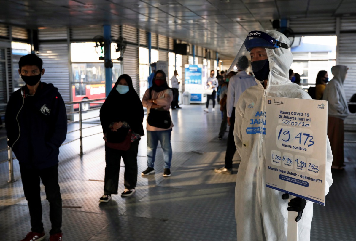 A worker wearing protective suit holds a placard with total positive cases of the coronavirus disease (COVID-19) written on it, at a central bus spot in Jakarta, Indonesia, July 27, 2020. REUTERS/Willy Kurniawan