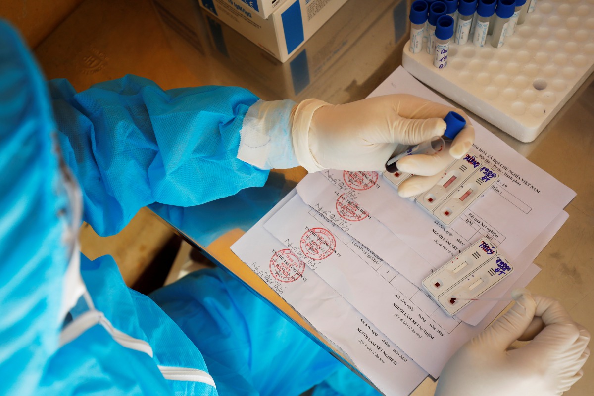 A medical specialist wearing a protective suit pours droplets of blood, collected from people who have returned from Da Nang, onto a test kit for coronavirus disease (COVID-19) at a rapid testing center outside Hanoi, Vietnam July 30, 2020. REUTERS/Kham