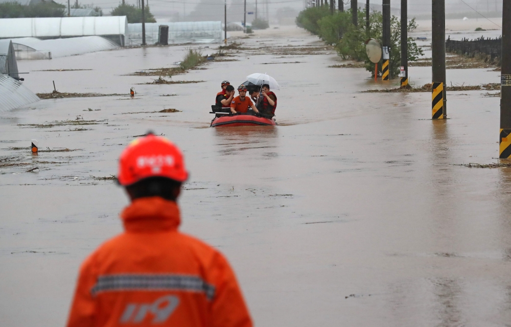 In a photo taken on August 3, 2020 rescue services help people cross a flooded field in a village near Cheonan, following heavy rain. Damage from heavy rain that pounded the country's central region earlier this week continued to grow, leaving 13 dead and