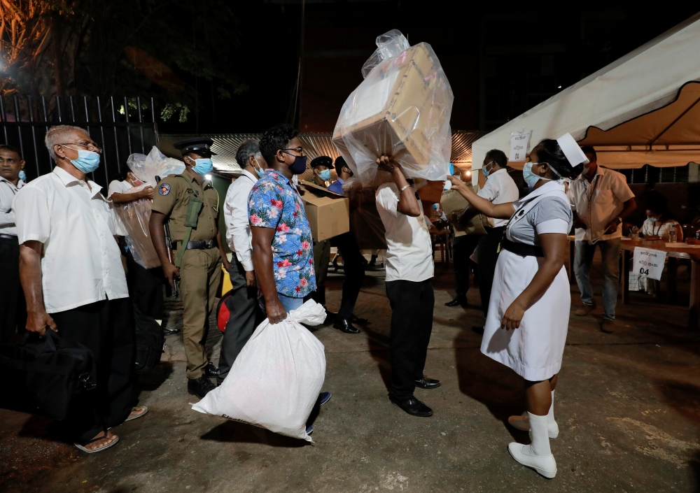 A health official takes the temperature of election officials who arrive with ballot boxes from a polling station to a counting center, after the voting ended during the country's parliamentary election in Colombo, Sri Lanka, August 5, 2020. REUTERS/Dinuk