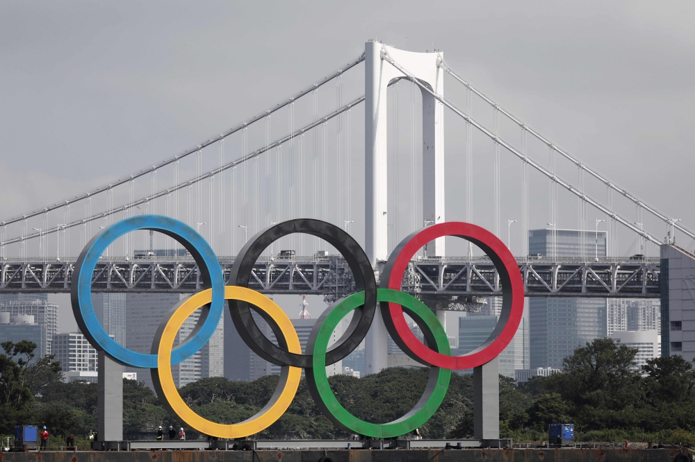 A large size Olympic rings symbol (W32.6m x H15.3m) is seen in front of Rainbow Bridge at Tokyo Waterfront in the waters of Odaiba Marine Park on August 6, 2020 before being transferred back to the factory where it was manufactured for a safety inspection