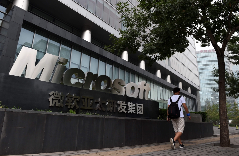 This file photo taken on July 31, 2014 shows a man walking past a Microsoft sign outside a Microsoft office building in Beijing. / AFP / Greg Baker
