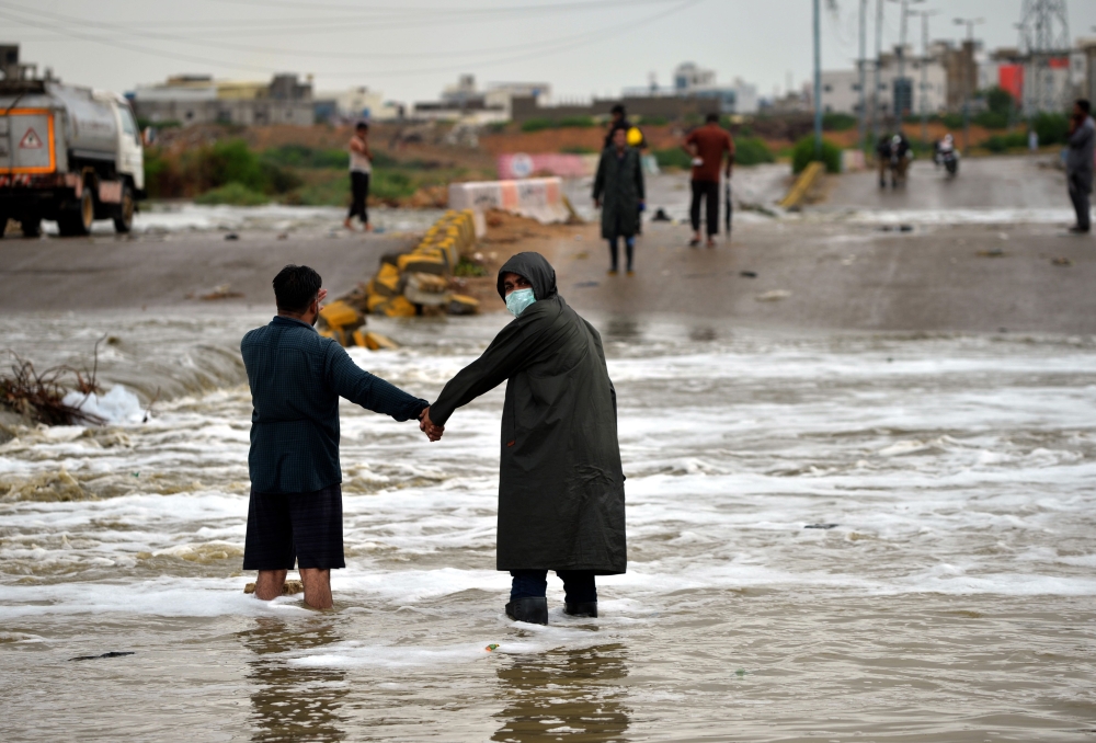 Commuters make their way along a flooded road after a monsoon rain in Pakistan's port city of Karachi on August 8, 2020. / AFP / Rizwan TABASSUM