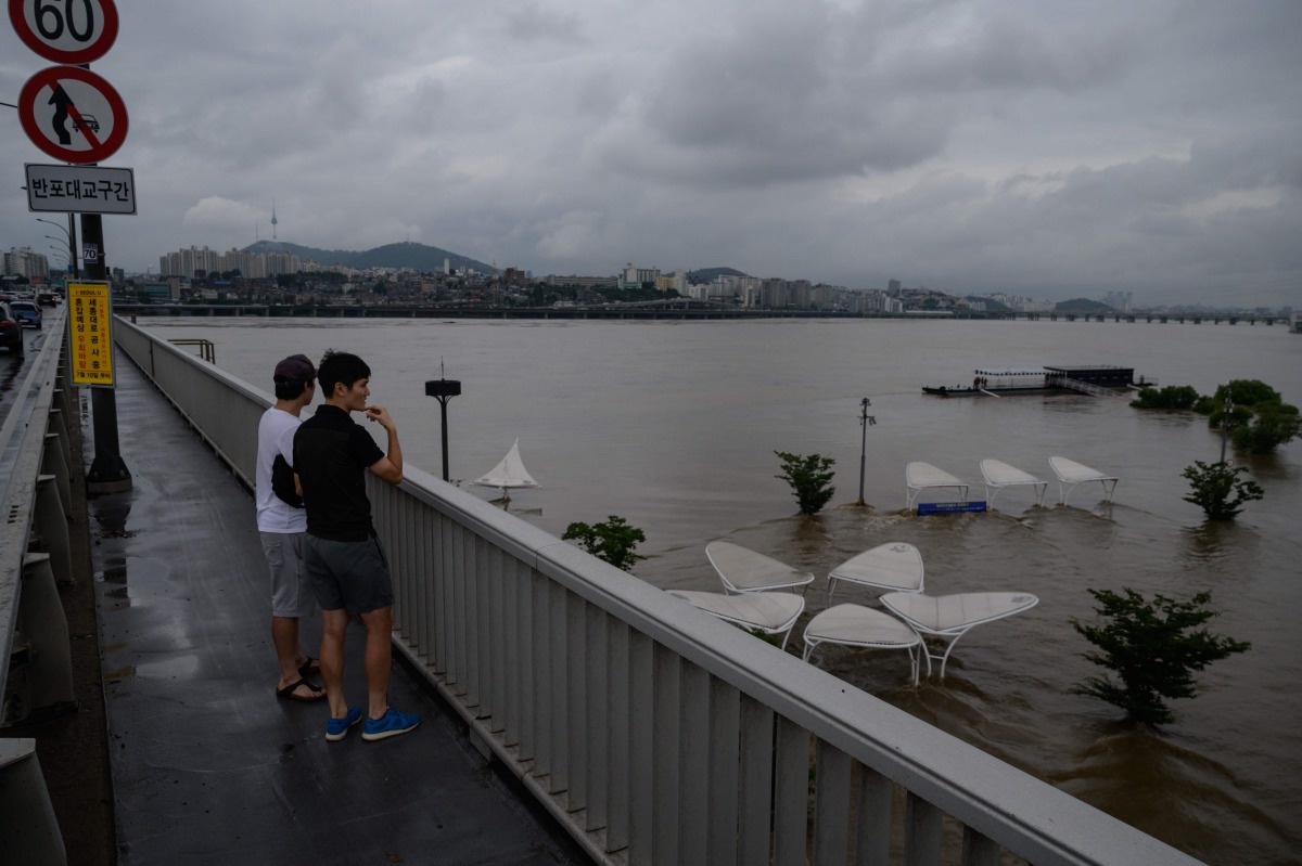 Pedestrians stand on a bridge as they look at a park inundated by flood water beside the Han river in Seoul on August 3, 2020. Heavy rain hit South Korea's central regions causing flooded houses and roads, Yonhap news agency reported, prompting authoritie