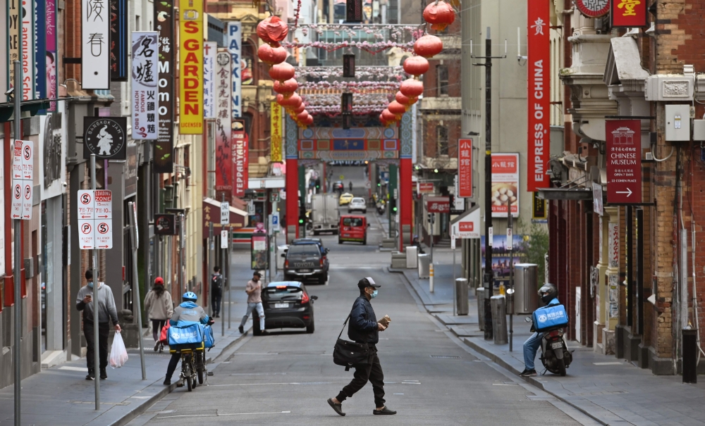A man wearing a face mask crosses a quiet road in Melbourne's Chinatown area on August 13, 2020. Australia's virus-hit Victoria state reported a major drop in new coronavirus cases on August 13, but officials warned against complacency amid a 