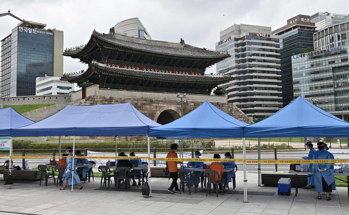 Health workers wearing protective clothing receive people at a temporary COVID-19 coronavirus testing station near Namdaemun (background), a 600-year-old gate listed as South Korea's number one national treasure, in Seoul on August 10, 2020. / AFP / Jung 