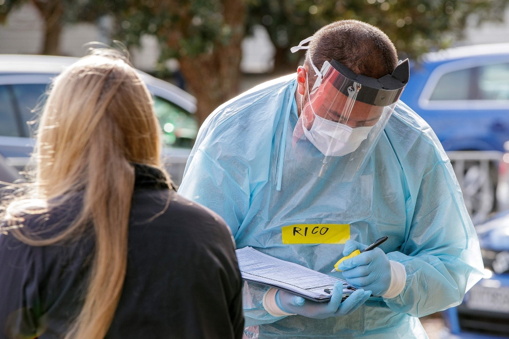 A health worker takes details at a COVID-19 testing station setup at Eden Park, National Sports Stadium, in Auckland on August 14, 2020.  / AFP / DAVID ROWLAND