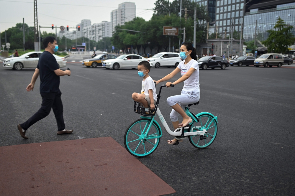 A woman and child wearing face masks commute on a public share bicycle on a street in Beijing on August 20, 2020. (AFP / WANG ZHAO)