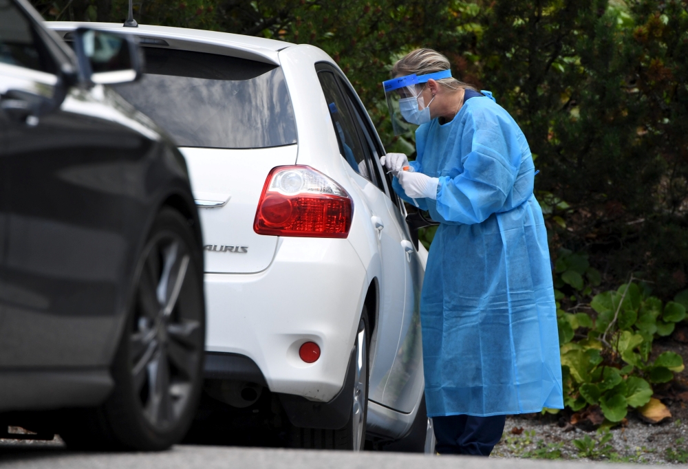 A medical worker wearing a protective suit and a mask takes a swab sample for a coronavirus disease (COVID-19) test at a drive-through testing station in Salo, Finland August 18, 2020. Lehtikuva/Jussi Nukari via REUTERS