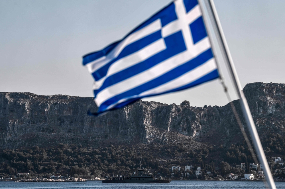 The Hellenic Navy Roussen or Super Vita class Fast Missile Patrol Boat P 71 HS Ritsos patrols off the tiny Greek island of Kastellorizo (Megisti) in front of a Greek flag, in the Dodecanese, the furthest south eastern Greek Island, two kilometers from the