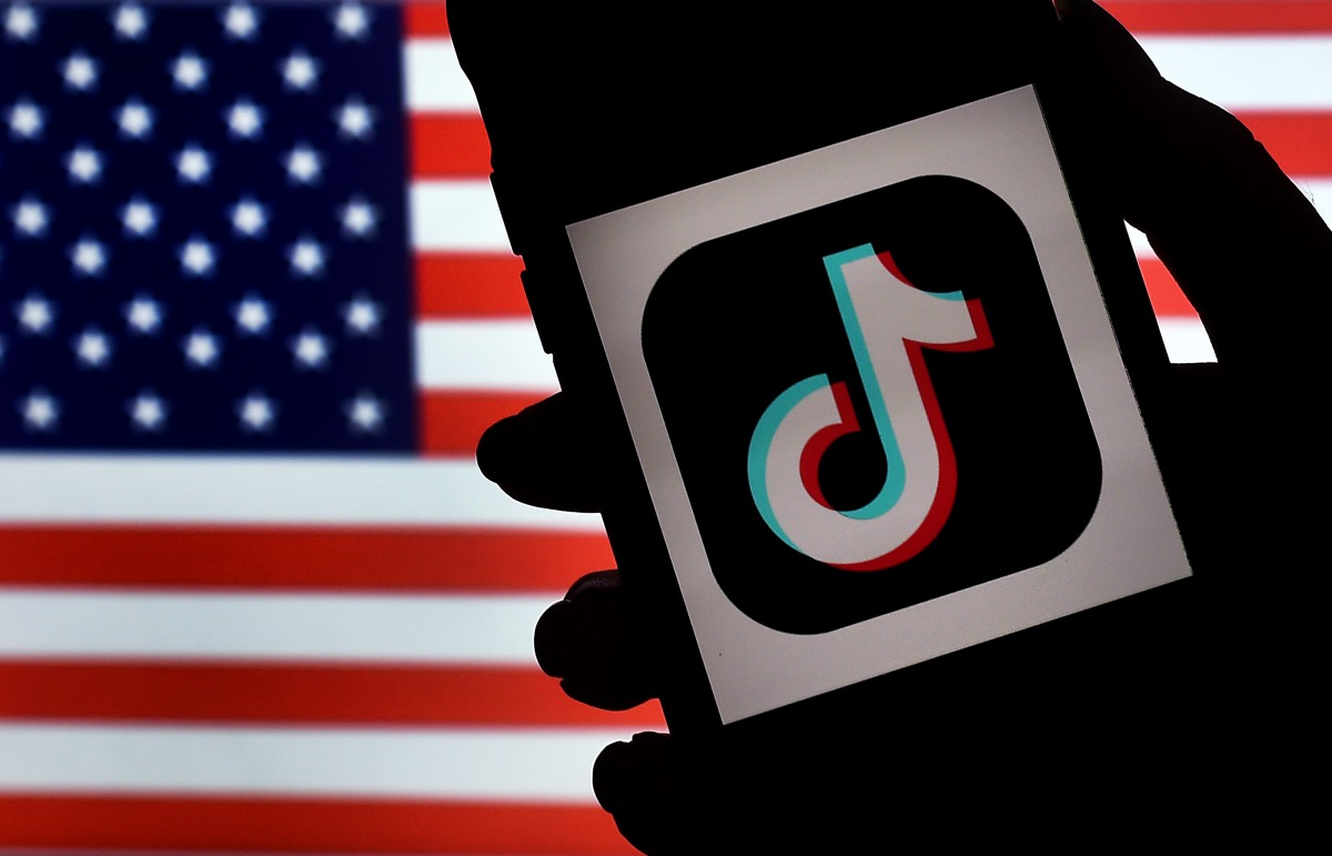 :(FILES) In this file photo illustration taken on August 3, 2020, the social media application logo, TikTok is displayed on the screen of an iPhone on an US flag as the background in Arlington, Virginia. President Donald Trump on September 21, 2020 threw 