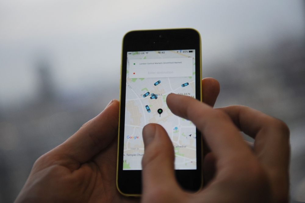 In this file photo taken on October 28, 2016 a man poses holding a smartphone showing the App for ride-sharing cab service Uber in London. Uber, September 28, wins appeal for new operating licence in London. / AFP / DANIEL SORABJI