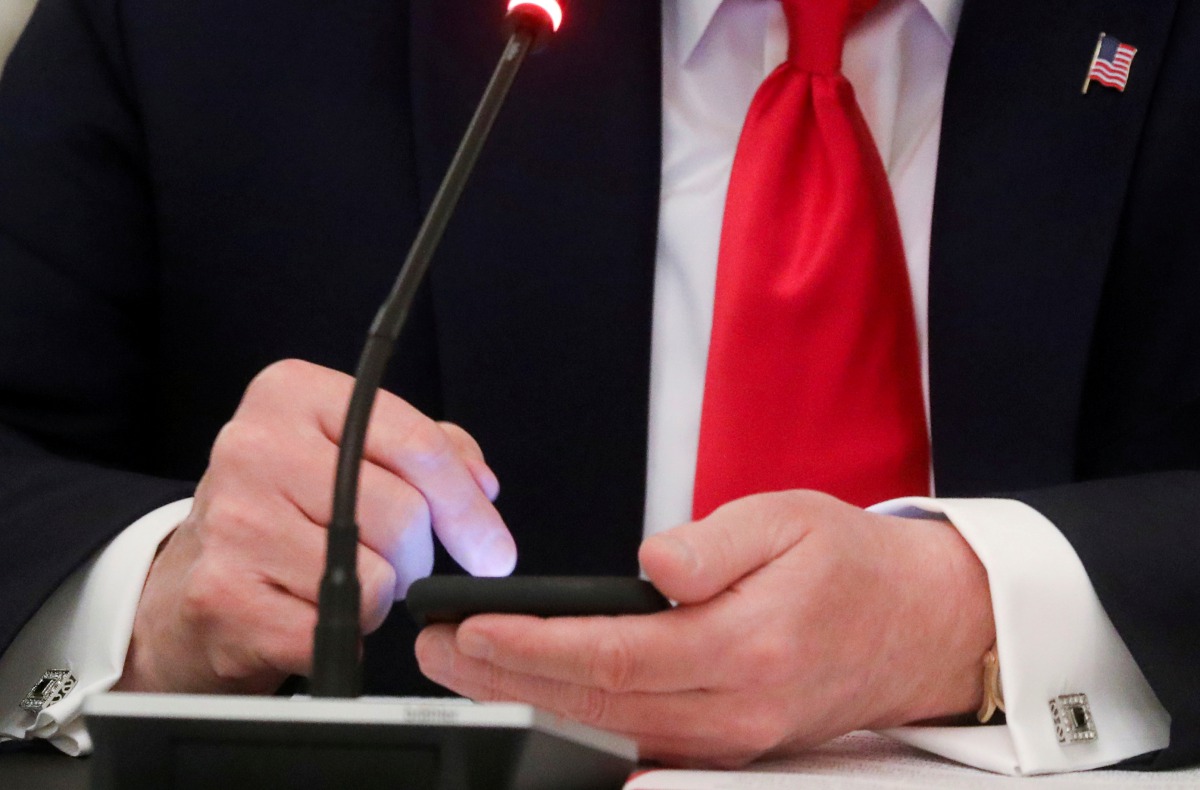 FILE PHOTO: U.S. President Donald Trump taps the screen on a mobile phone at the approximate time a tweet was released from his Twitter account, during a roundtable discussion on the reopening of small businesses in the State Dining Room at the White Hous