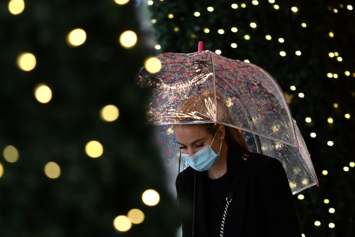A pedestrian wearing a face mask shelters under an umbrella as she passes a Christmas light display at a department store in central London on October 29, 2020. / AFP / JUSTIN TALLIS
