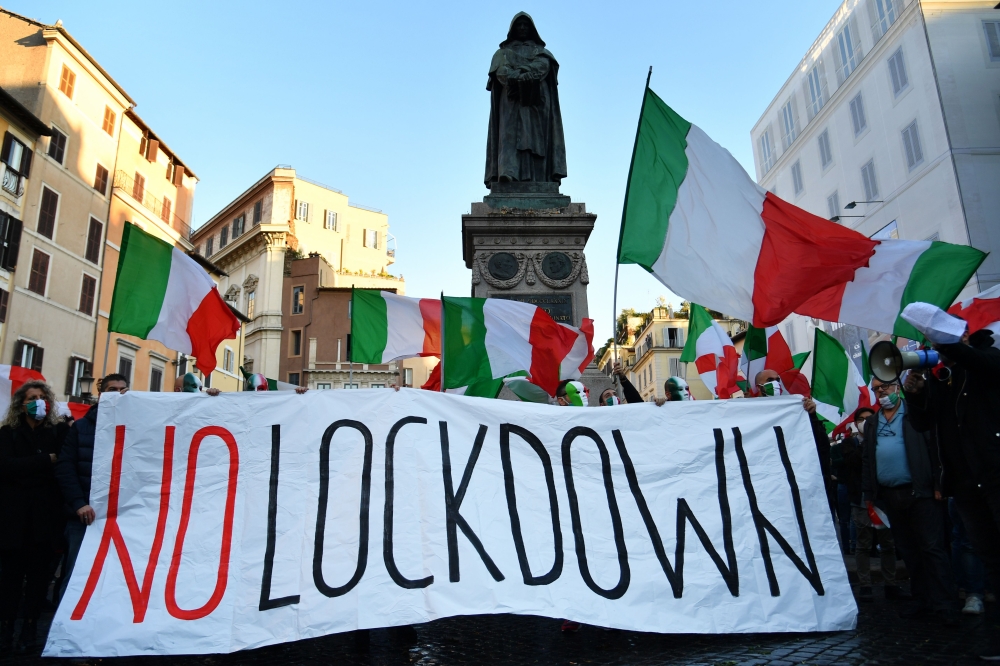 Protestors, wearing masks in the colors of the Italian flag, wave flags and a banner reading 