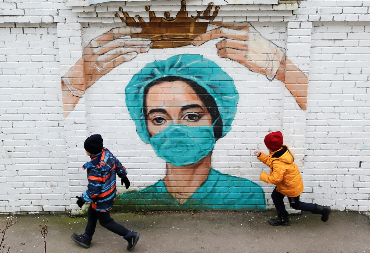 Children run past coronavirus-themed graffiti depicting a medic outside Saint Petersburg, Russia November 14, 2020. REUTERS/Anton Vaganov
