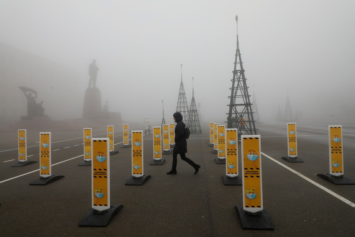 Pedestrians walk near near a skating rink past signs requesting to wear protective face masks and to keep a social distance amid the coronavirus disease (COVID 19) outbreak, as heavy fog covers a square named after Soviet state founder Vladimir Lenin in S