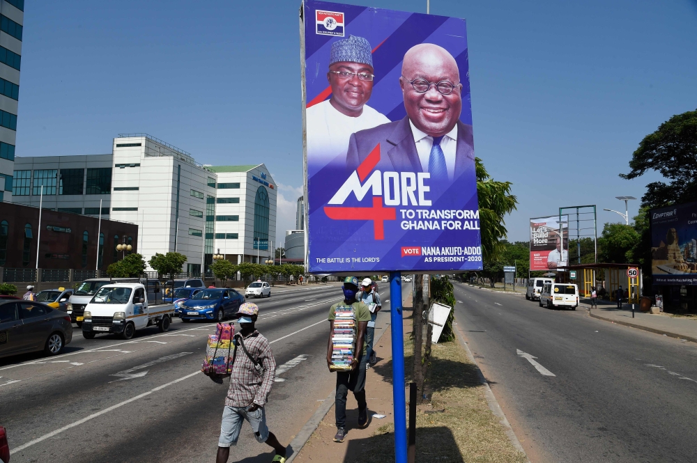 Street vendors walk past campaign posters of Ghanian President and candidate of the ruling New Patriotic Party (NPP) Nana Akufo-Addo and his running mate, Mahamudu Bawumia, in Accra, on December 4, 2020.  AFP / PIUS UTOMI EKPEI
