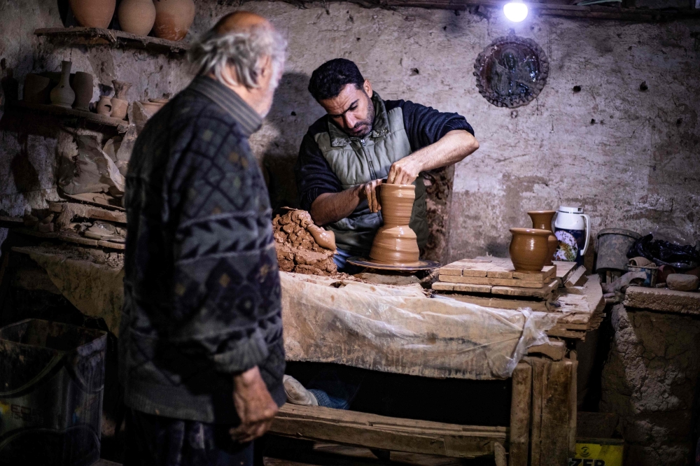Syrian-Armenian potter Misak Antranik Petros watches his son Anto moulding a clay vase at his workshop located inside an ancient mud-brick house near the city of Qamishli in Syria's northeastern Hasakeh province, on December 19, 2020. AFP / Delil Souleima
