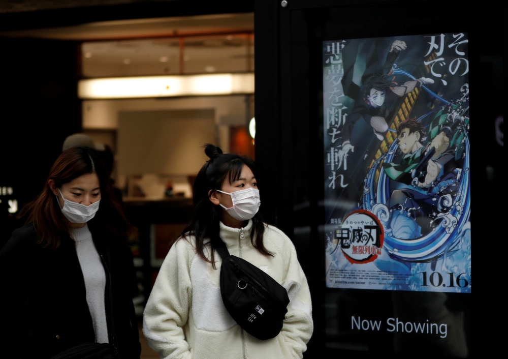File photo: Women wearing protective masks amid the coronavirus disease (COVID-19) outbreak walk past a poster for an animated movie 