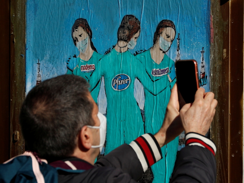 A man records a video of a painting representing Moderna, Pfizer and AstraZeneca vaccines at Bisbe street, during the coronavirus disease (COVID-19) outbreak, in Barcelona, Spain, January 27, 2021. REUTERS/ Albert Gea 